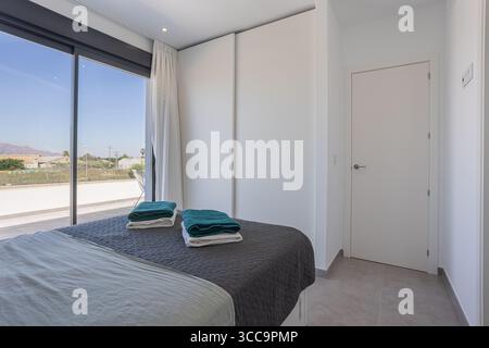 Chambre spacieuse aux lignes épurées, portes vitrées coulissantes qui s''ouvrent sur une terrasse avec vue sur les montagnes et les environs. Banque D'Images