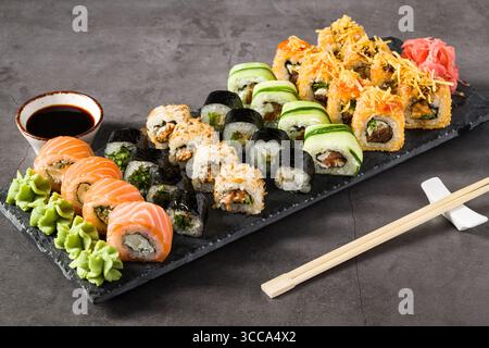 Assortiment de rouleaux de sushi servis sur une assiette en ardoise avec wasabi, sauce soja et gingembre Banque D'Images