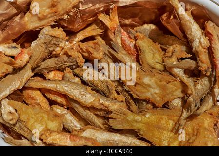 Un mélange de petits poissons frits dorés se trouve sur du papier brun, leur revêtement croquant et texturé et des formes variées reflétant les fruits de mer rustiques du sud de l'Italie Banque D'Images