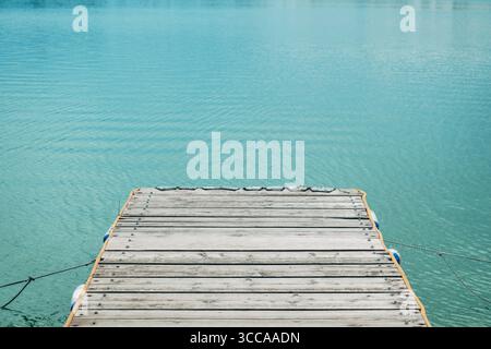 Jetée en bois s'étendant au-dessus de l'eau turquoise calme par une journée ensoleillée brillante. Mise au point sélective. Banque D'Images