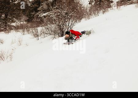 Les garçons ont traîné en traîneau sur une colline enneigée dans le plaisir de la forêt d'hiver Banque D'Images