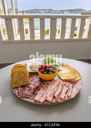 Brunch de style méditerranéen ou assiette de hors-d'œuvre avec assortiment de viandes, fromages et légumes servis en plein air sur une terrasse au bord de la mer Banque D'Images
