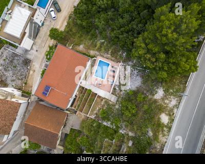 Vue aérienne des toits en terre cuite rencontre l'étreinte turquoise d'une piscine privée nichée au milieu d'arbres verdoyants, un havre de paix baigné de soleil, Drvenik, comté de Split-Dalmatie, Croatie. Banque D'Images
