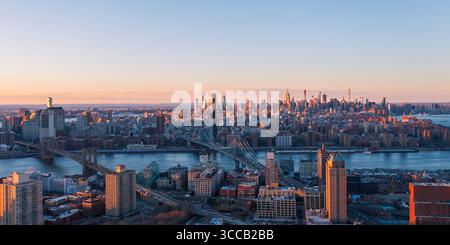 Vue aérienne des ponts enjambant la rivière vers une ligne d'horizon lointaine avec l'Empire State Building attrapant la lueur chaude du soleil couchant, New York, U. Banque D'Images