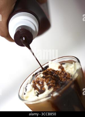 L'ajout de sirop de chocolat et crème d'une secousse de glace Banque D'Images