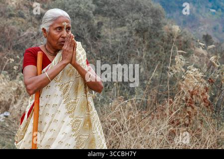 Chandanath hill, Bangladesh - 12 March 2021: View of an elderly woman in traditional attire, hands clasped in prayer, standing amidst the serene, muted landscape. Banque D'Images