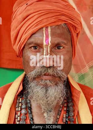Chandanath hill, Bangladesh - 12 March 2021: View of a weathered sadhu with a saffron turban, his gaze intense, face painted with sacred marks. Banque D'Images