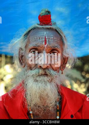 Chandanath hill, Bangladesh - 12 March 2021: View of a weathered sadhu with a striking red mark on his forehead, his gaze intense against a serene blue backdrop. Banque D'Images