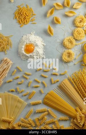 Différents types de pâtes disposées en cercle avec de la farine et du jaune d'œuf au centre, créant une vue aérienne des ingrédients de la cuisine italienne Banque D'Images
