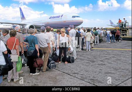 Britannia Thomson Boeing jet Airliner fournit une toile de fond aux voyageurs de vacances de retour à la maison en 1998 archive vue arrière des passagers dans les modes de voyage des années 90 avec des bagages à main faisant la queue pour embarquer à bord d'un avion jet pour un vol de retour sans escale à Gatwick Londres Royaume-Uni au départ de cet aéroport de Santo Domingo des années 90 en République dominicaine surveillé par l'équipage au sol une image d'archives de la façon dont nous étions à l'époque dans les années 1990 Banque D'Images