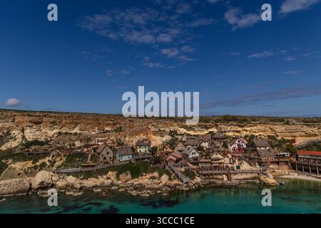 Vue sur Popeye Village à Anchor Bay, Malte, par une journée ensoleillée avec un ciel bleu vif, capturant le village coloré et le littoral. Banque D'Images