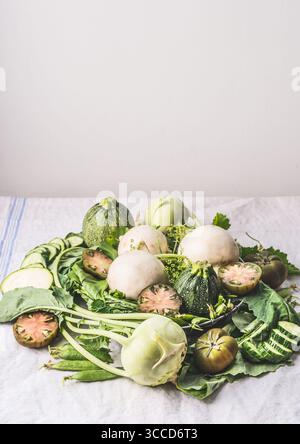 Tas de divers légumes ferme bio de saison vert pour la cuisine végétarienne savoureuse sur la lumière table de cuisine. Style rustique. La saine alimentation et de la cuisine Banque D'Images