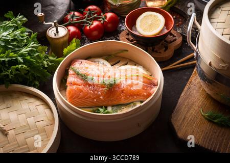 Filet de saumon cru en bateau à vapeur de bambou foncé sur table de cuisine rustique avec des ingrédients et des outils. La saine alimentation et de la cuisine. Concept de suivre un régime. Cuisine asiatique Banque D'Images