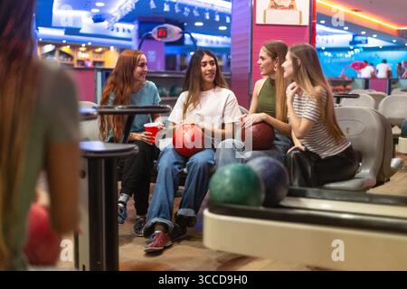 Quatre jeunes femmes jouissant d'une partie amicale de bowling, bavardant et s'amusant ensemble à la piste de bowling Banque D'Images