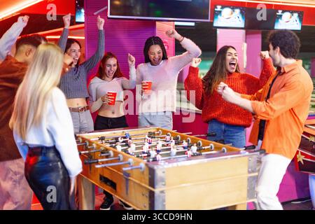 Groupe d'amis excités acclamant et célébrant tout en jouant au baby-foot dans une piste de bowling Banque D'Images