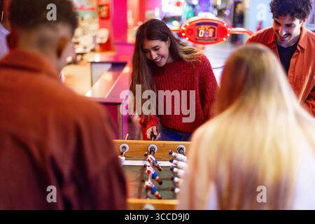 Groupe d'amis profitant d'un jeu animé de baby-foot dans une arcade d'amusement, rempli de lumières colorées et d'excitation joyeuse Banque D'Images