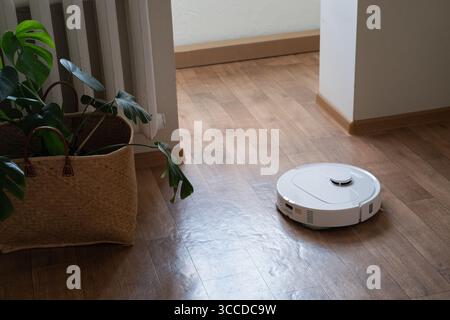 Aspirateur robot de nettoyage moderne sans effort nettoie le sol dans un intérieur lumineux de la maison, économisant du temps et de l'énergie pour le propriétaire. Banque D'Images