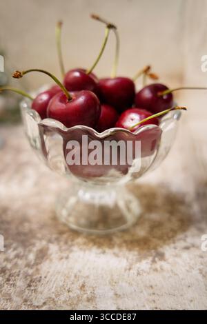 Des cerises fraîchement cueillies débordant d'un bol en verre, créant un affichage vibrant sur une table rustique Banque D'Images