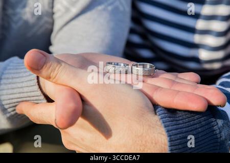Un couple aimant exprime son engagement en tenant des anneaux de mariage dans leurs mains un jour ensoleillé d'automne. Banque D'Images