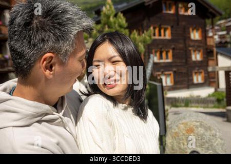 Couple asiatique profite d'un moment romantique ensemble dans un charmant village de montagne, avec des maisons traditionnelles en bois en arrière-plan Banque D'Images