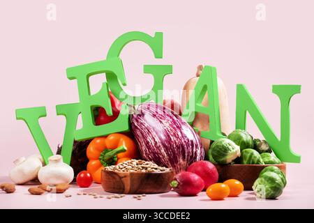 Le mot VEGAN en grandes lettres vertes sur la table rose, entouré de fruits frais, légumes et un bol de lentilles, régime végétalien nature morte Banque D'Images