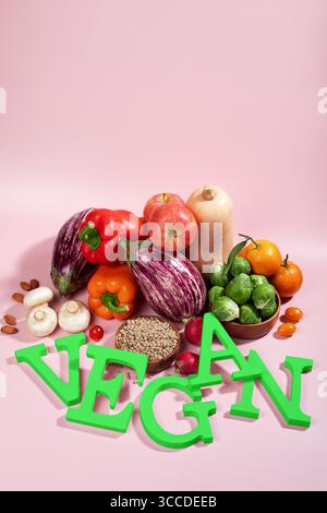 Le mot VEGAN en grandes lettres vertes sur la table rose, entouré de fruits frais, légumes et un bol de lentilles, régime végétalien nature morte Banque D'Images