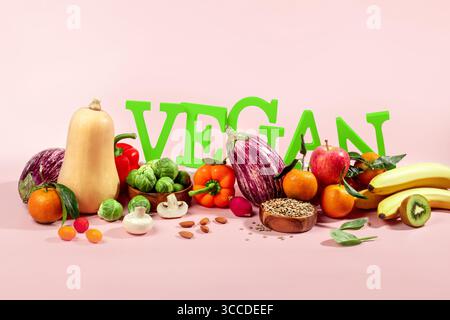Le mot VEGAN en grandes lettres vertes sur la table rose, entouré de fruits frais, légumes et un bol de lentilles, régime végétalien nature morte Banque D'Images
