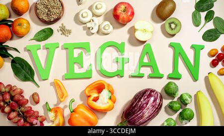Le mot VEGAN en grandes lettres vertes sur la table beige, entouré de fruits frais, légumes et un bol de lentilles, végétalien plat de régime Banque D'Images