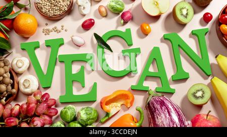 Le mot VEGAN en grandes lettres vertes sur la table beige, entouré de fruits frais, légumes et un bol de lentilles, végétalien plat de régime Banque D'Images