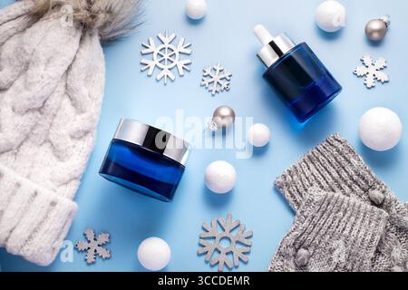 Produits de beauté de soins de la peau d'hiver et accessoires d'hiver doux comme chapeau de laine et moufles, tous disposés sur fond bleu, concept de surf de soins de la peau d'hiver Banque D'Images