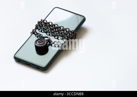 Téléphone portable se trouve sur fond blanc enveloppé avec chaîne en métal avec serrure sur le thème de sécurité et de protection des données Banque D'Images