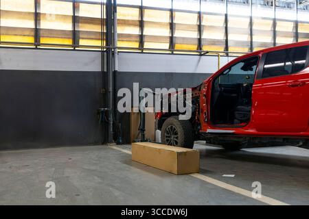 Photo d'un véhicule 4x4 rouge en réparation avant dans un garage propre avec boîte et équipement à proximité Banque D'Images