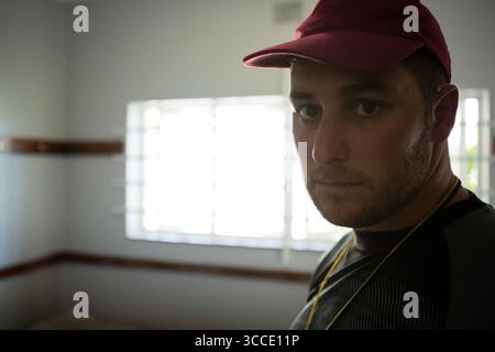 La casquette de baseball rouge et la lanière jaune sont suspendues près de la fenêtre barrée lumineuse, au-dessus des garnitures en bois. Portrait, tenue vestimentaire, décontracté, minimaliste, espace de travail, professe Banque D'Images