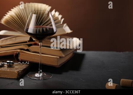 Vin rouge en verre et livres sur table texturée sombre sur fond brun, gros plan. Espace pour le texte Banque D'Images