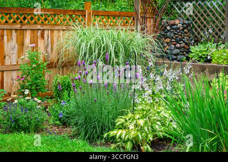 Jardin d'angle avec clôture et lanerne éclairée au milieu de belles fleurs d'été sous la pluie. Banque D'Images