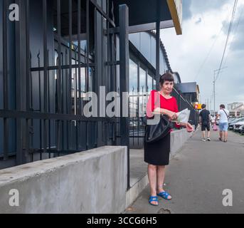 Kiev, Ukraine - 25 juillet 2025 : une femme âgée est debout sur le trottoir devant un magasin fermé à Kiev, Ukraine, tenant un sac d'épicerie Banque D'Images