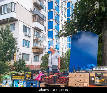 Kiev, Ukraine - 25 juillet 2025 : femme âgée debout à côté de caisses de fruits et légumes qu'elle vend dans un marché en plein air à Kiev, Ukraine, wit Banque D'Images