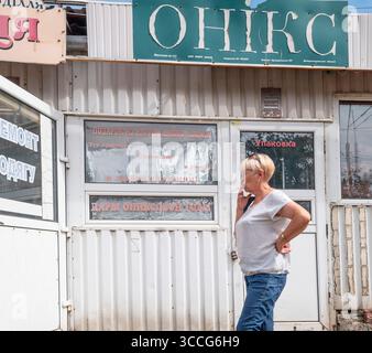 Kiev, Ukraine - 25 juillet 2025 : une femme âgée fume une cigarette alors qu'elle se tient à côté d'un petit magasin à Kiev, Ukraine, montrant un aperçu de la maladie Banque D'Images
