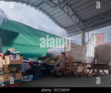 Kiev, Ukraine - 25 juillet 2025 : vendeuse de rue assise dans une chaise à son étal dans le marché extérieur de Kiev, entourée de marchandises sous une bâche verte Banque D'Images