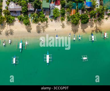 Plage de Port Barton avec de nombreux bateaux philippins traditionnels sur le littoral. Vue aérienne drone de la plage de sable avec palmiers tropicaux. Palawan, Philippines Banque D'Images