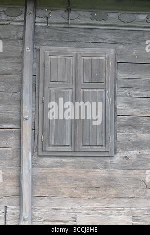 Mur en bois rustique présentant une texture vibrante et des volets fermés, soulignant la charmante simplicité et l'élégance de l'artisanat en bois. Banque D'Images