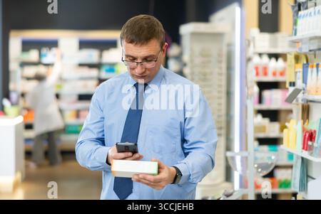 Dans la pharmacie visiteur masculin scanner le code à barres et lit la composition de la pommade médicinale Banque D'Images