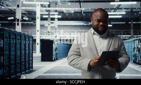 Travailleur en salle de serveurs dépannage des problèmes de connectivité du serveur à l'aide d'un logiciel sur tablette. Technicien de centre de données mettant à niveau le matériel des réseaux d'entreprise à l'aide de l'appareil, de la caméra A. Banque D'Images