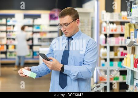 Dans la pharmacie visiteur masculin scanner le code à barres et lit la composition de la pommade médicinale Banque D'Images