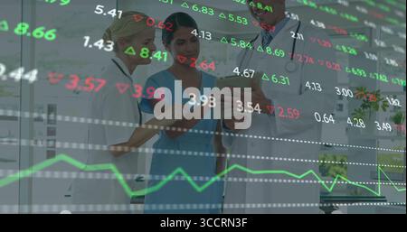 Équipe de conseil portant des gommages, des manteaux examinant la tablette au poste de soins infirmiers, avec des superpositions financières Banque D'Images