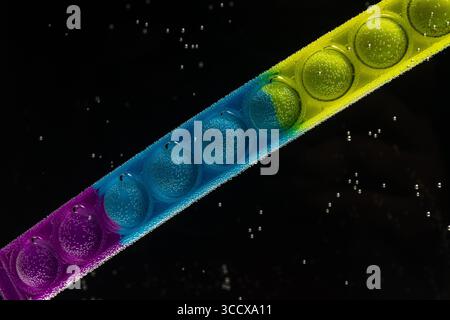 Une bande vibrante et multicolore, peut-être un jouet de fidget sensoriel comme un Pop It, positionné en diagonale contre un sombre Banque D'Images