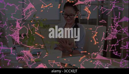 Femme asiatique souriante portant chemisier d'affaires tenant une tablette dans un bureau moderne, avec smartphone portable Banque D'Images