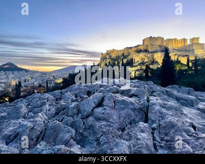 Lever de soleil sur la colline d'Areopagus avec la lumière chaude du matin illuminant l'Acropole et le paysage urbain d'Athènes. Banque D'Images