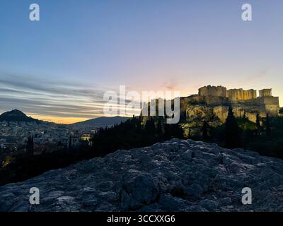 Lever de soleil sur la colline d'Areopagus avec la lumière chaude du matin illuminant l'Acropole et le paysage urbain d'Athènes. Banque D'Images
