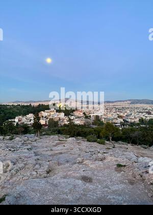 Vue du lever du soleil depuis la colline d'Areopagus avec le paysage urbain d'Athènes, mettant en valeur le bâtiment jaune et la montagne lointaine. Banque D'Images